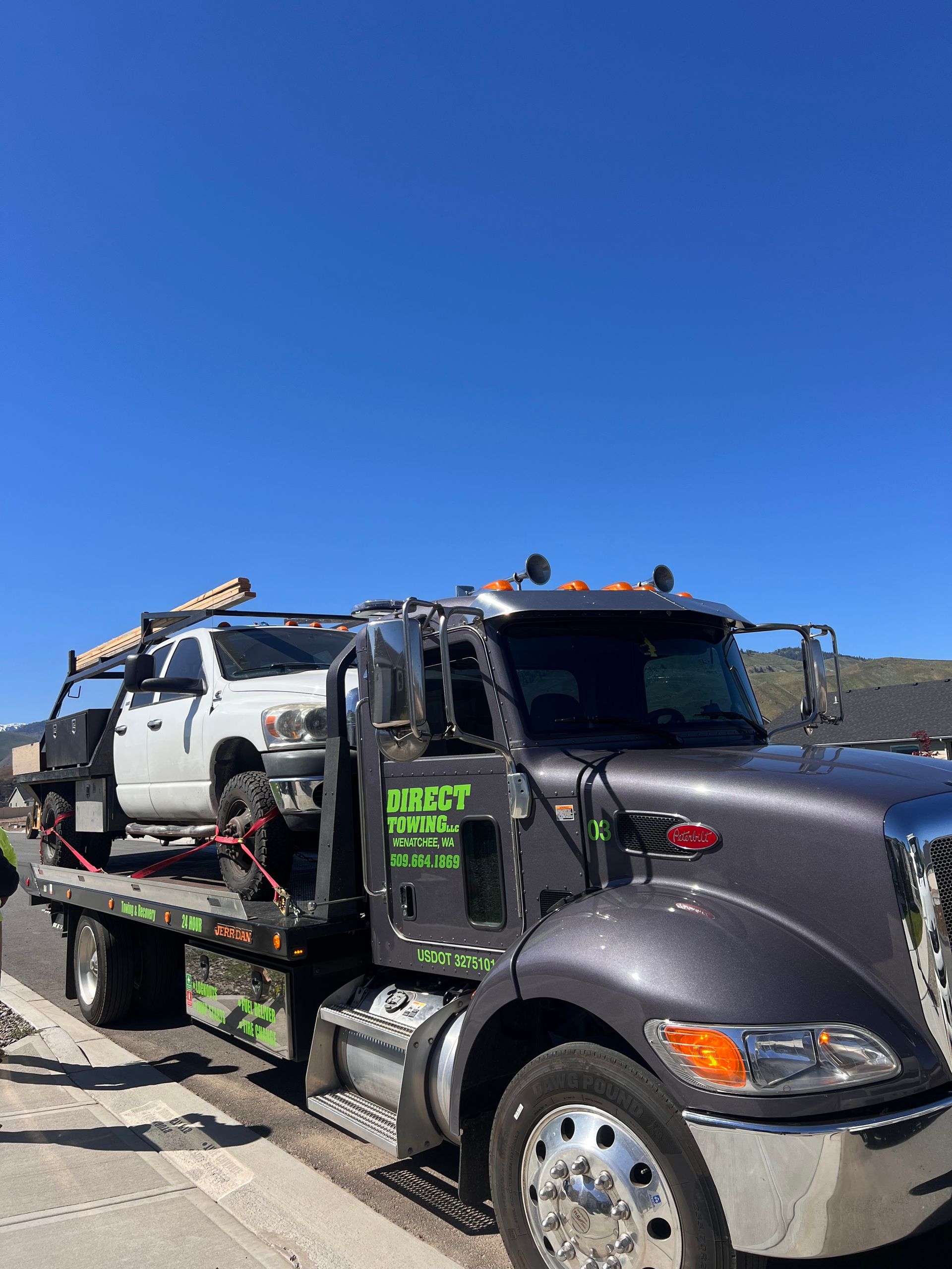 Tow truck carrying a white SUV on a sunny roadside under a clear blue sky