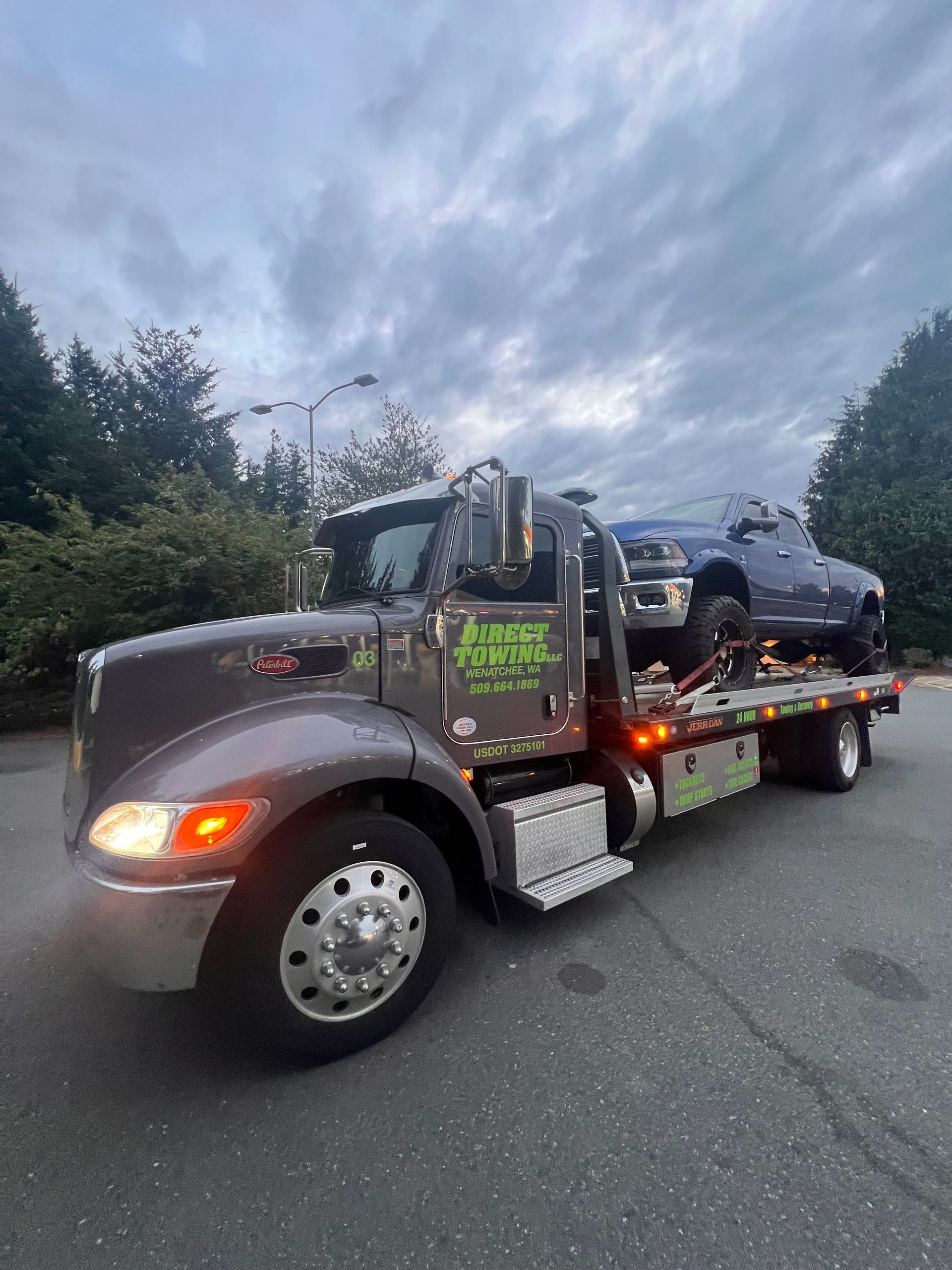 Tow truck hauling a gray SUV on a flatbed along a road at dusk