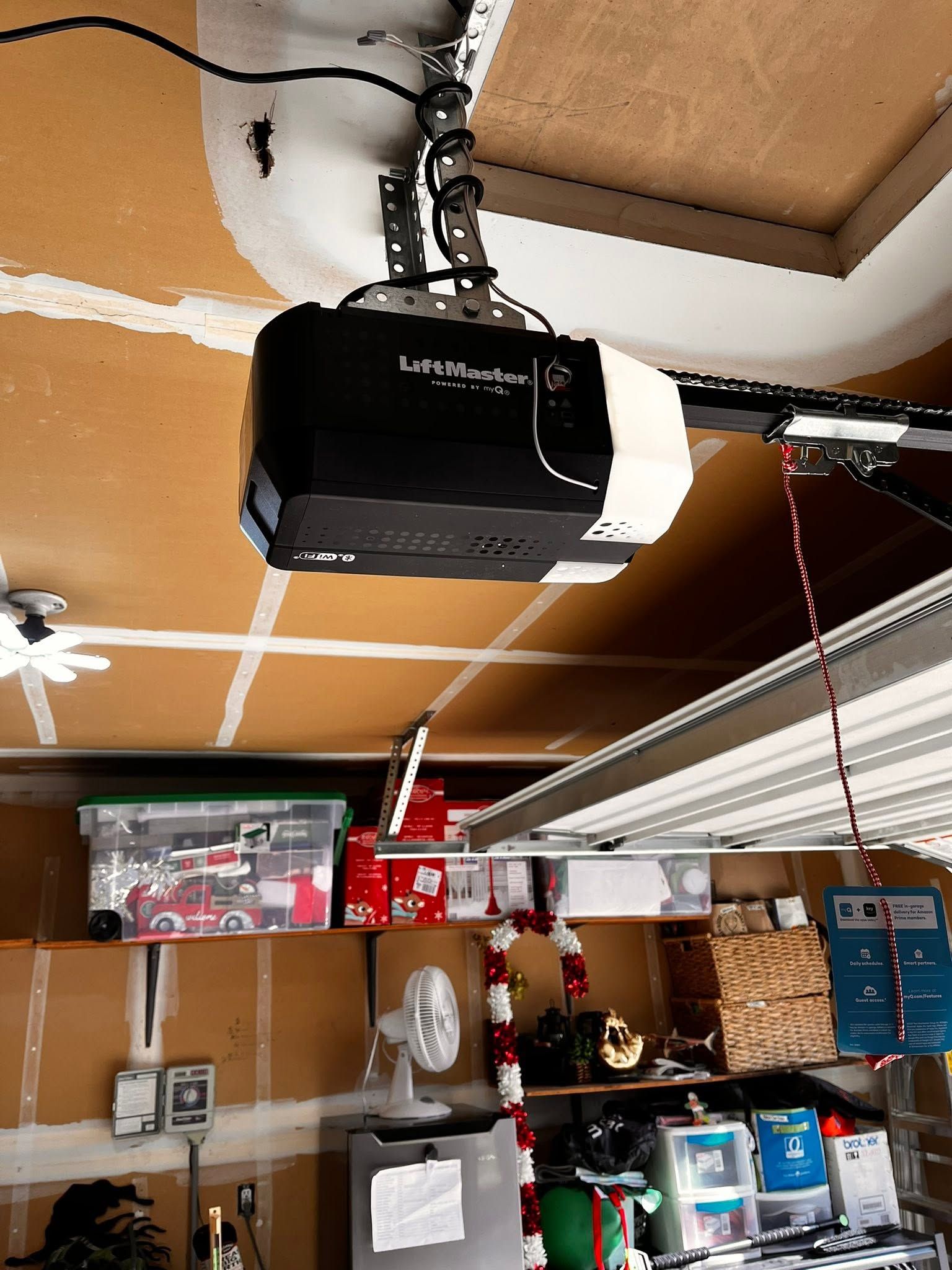 Garage ceiling with a black LiftMaster garage door opener and hanging cords over shelves below