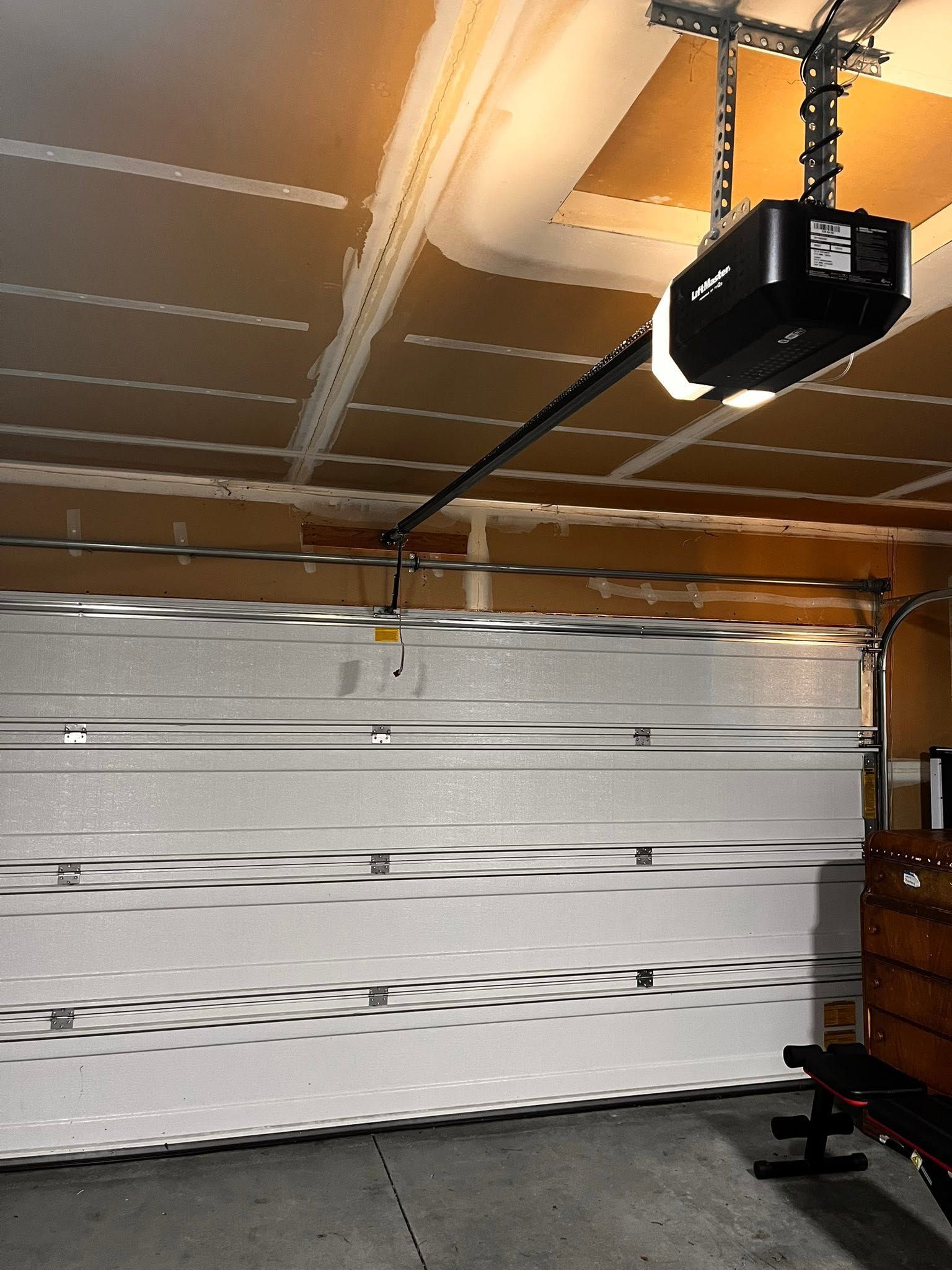 White sectional garage door with black opener in a garage interior, viewed from inside.