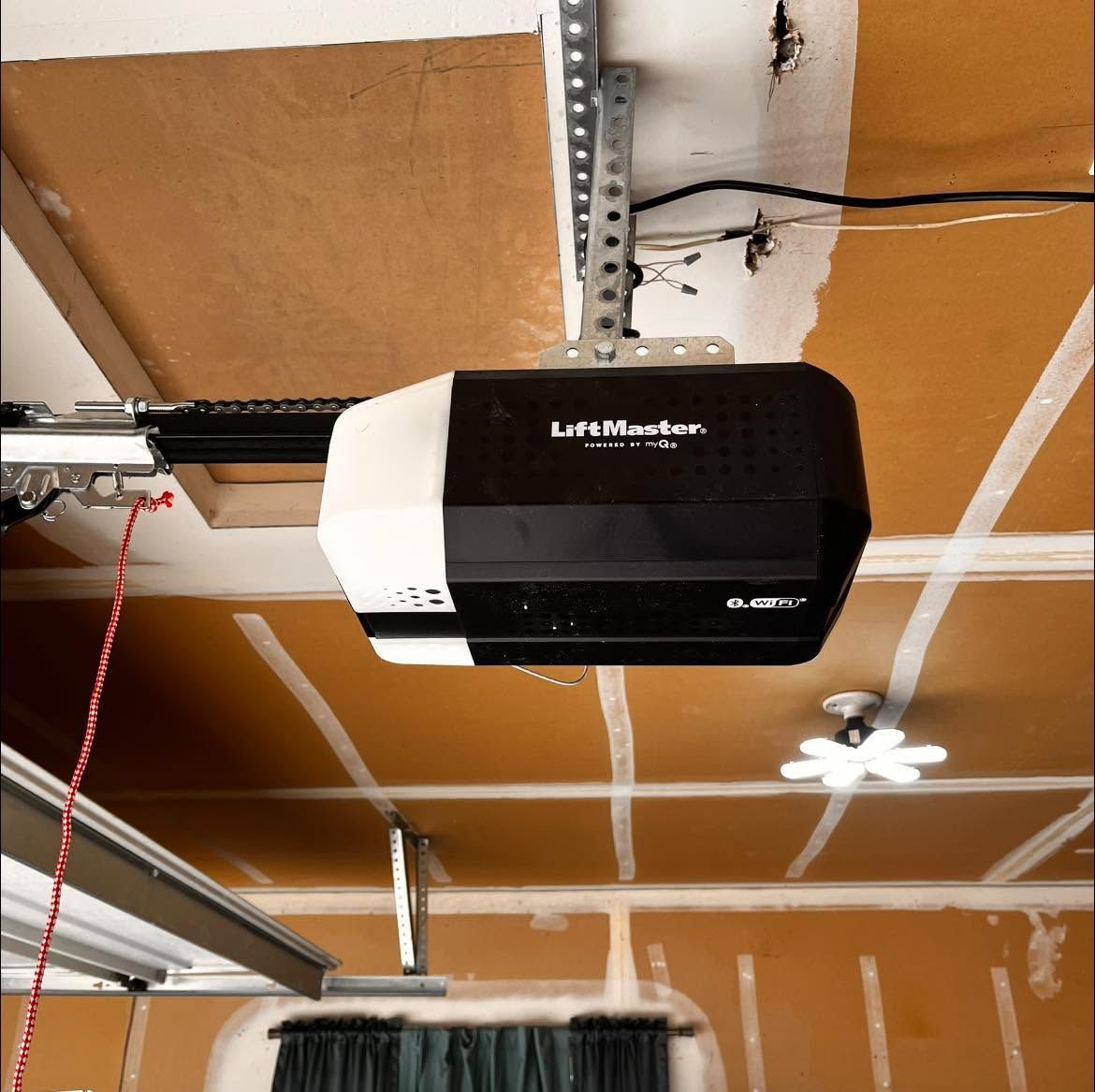 Black and white garage door opener mounted on a ceiling with exposed beams and garage door tracks