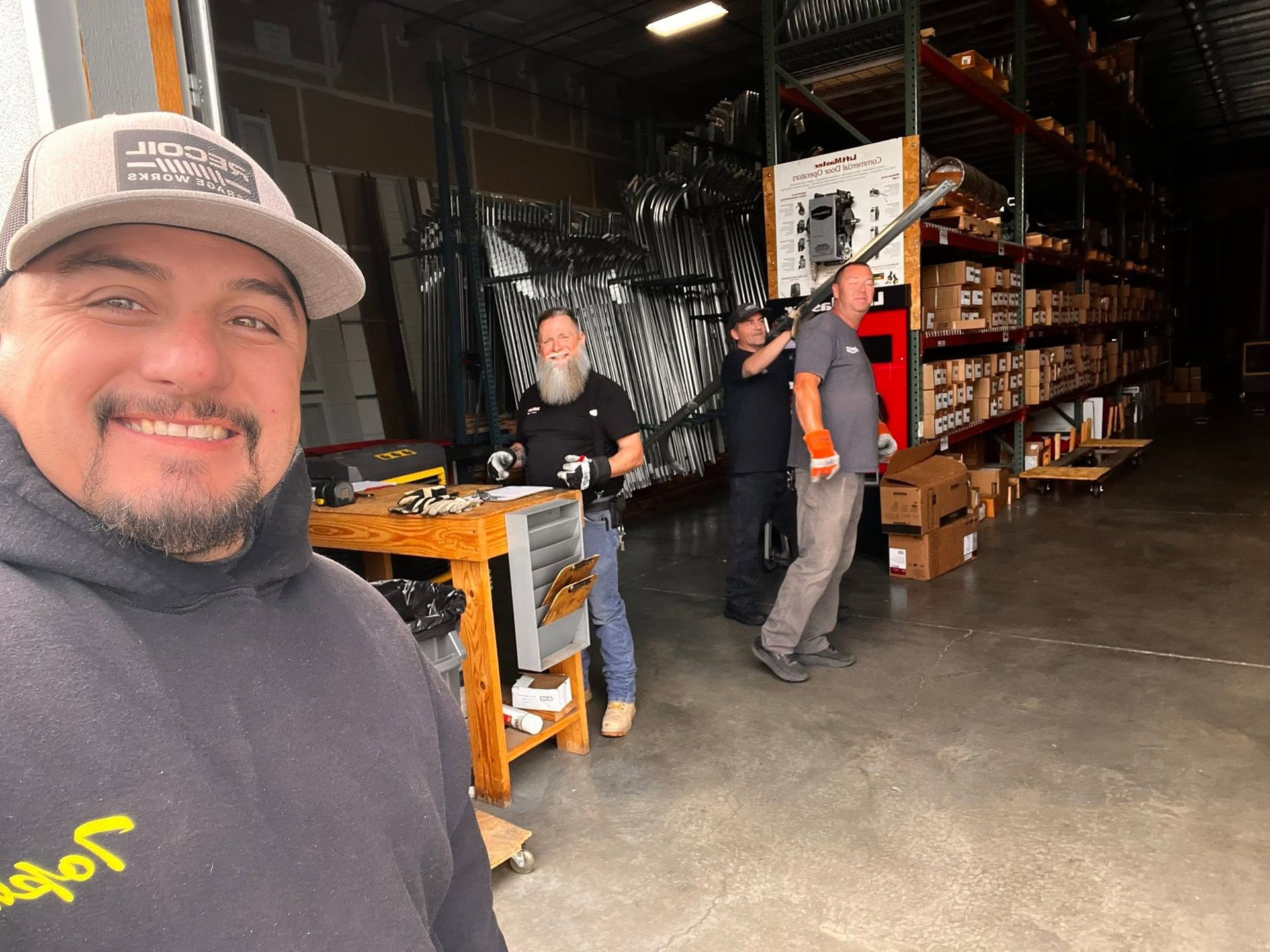 Selfie in a warehouse aisle with three people near shelves and equipment.