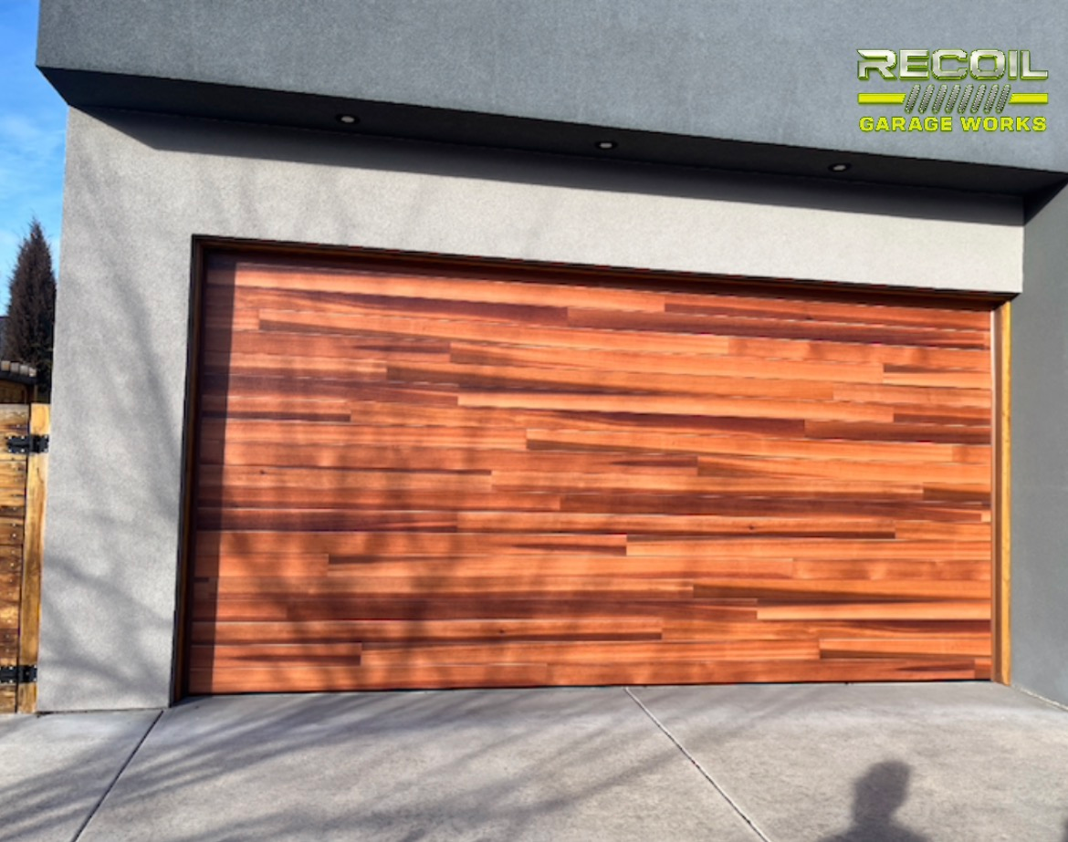 Modern garage with a wood-paneled door and gray stucco exterior in daylight