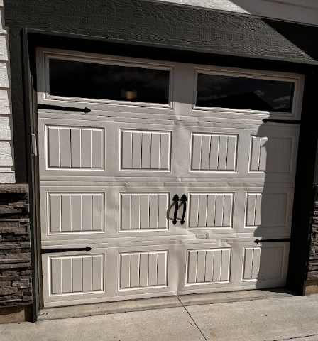 White garage door with window panels and dark handles on a house exterior