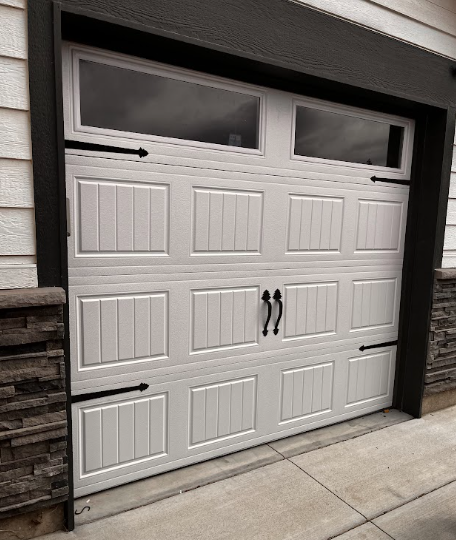 White paneled garage door with black handles and frosted windows in a stone-trimmed driveway