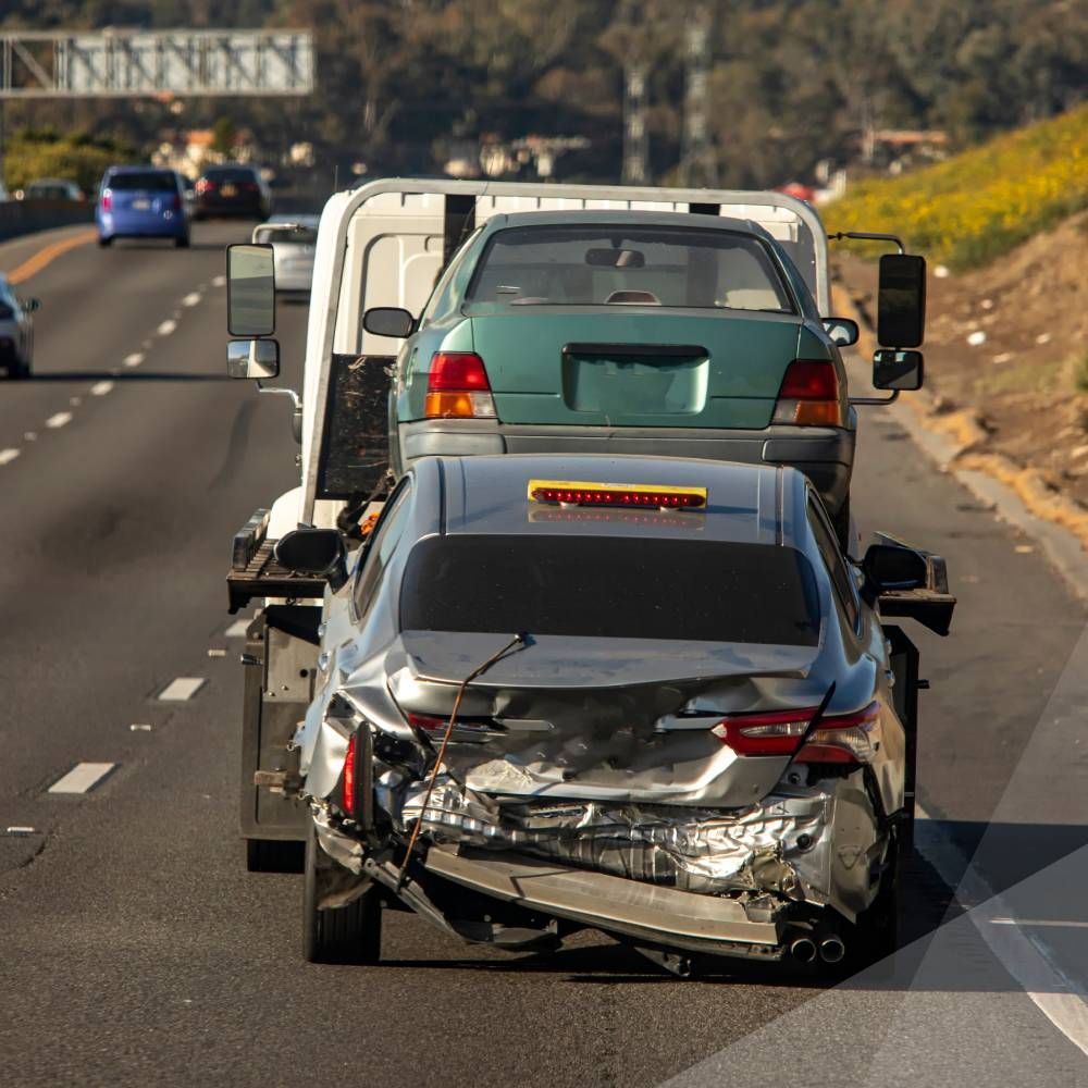 A tow truck is towing a damaged car on a highway