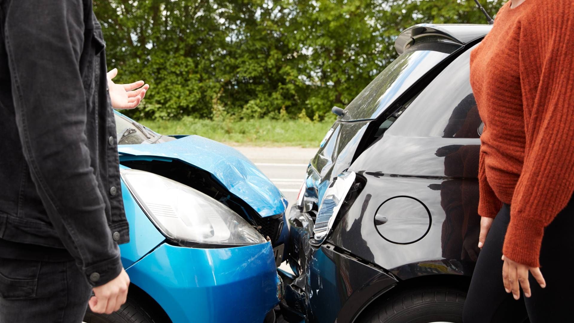 A man and a woman are standing next to two cars that have been involved in a car accident.