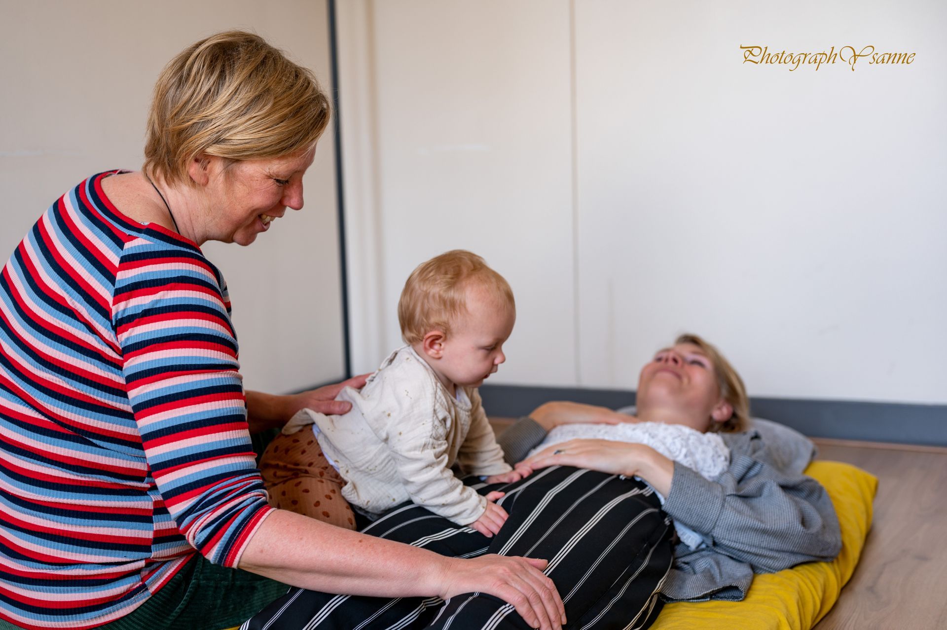 Een vrouw ligt op een gele deken met een baby op haar schoot.