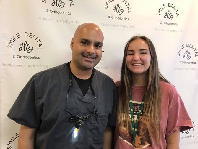 Two people smiling in front of a Smile Dental & Orthodontics backdrop