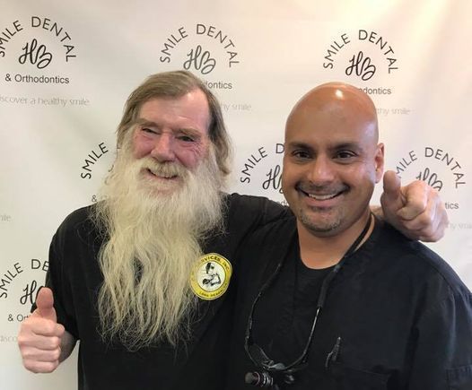 Two smiling men posing with thumbs up in front of a Smile Dental backdrop