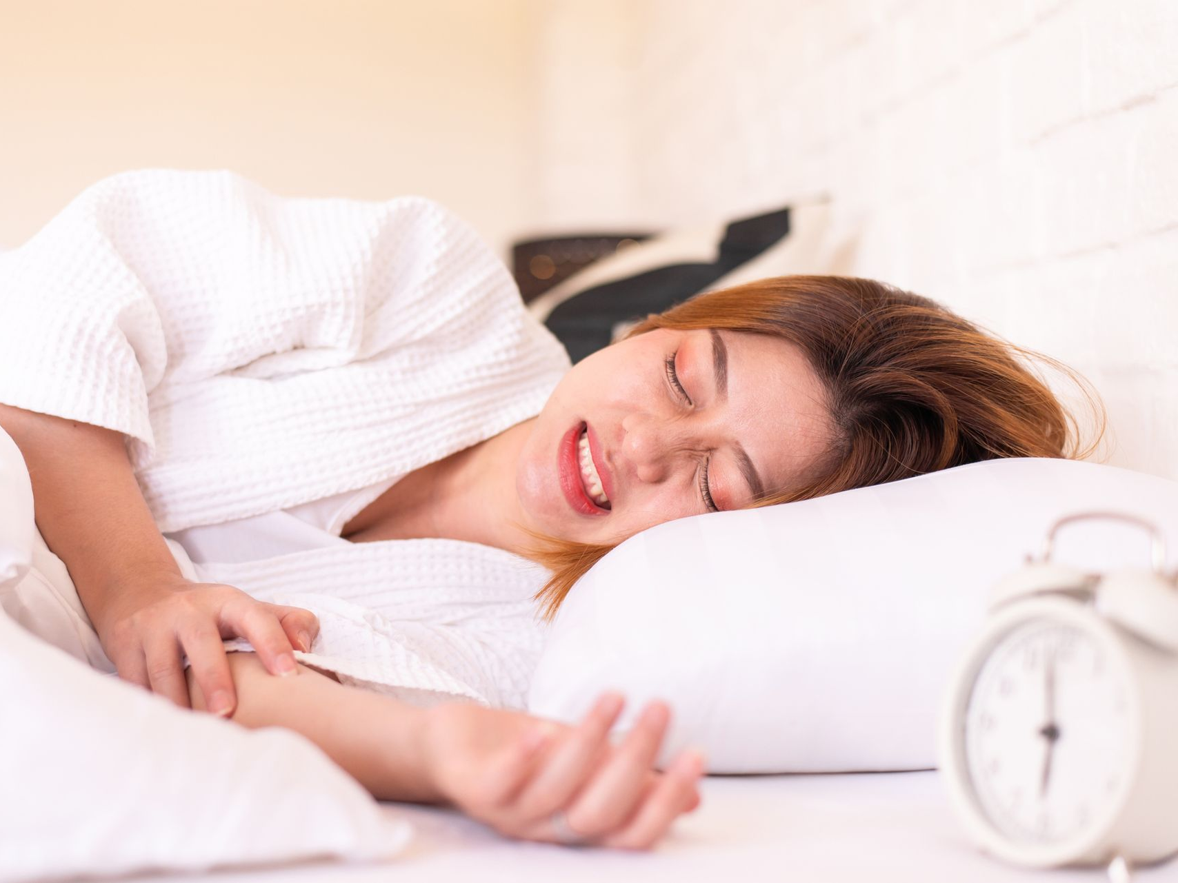 Person sleeping in a white robe on a pillow, with an alarm clock nearby