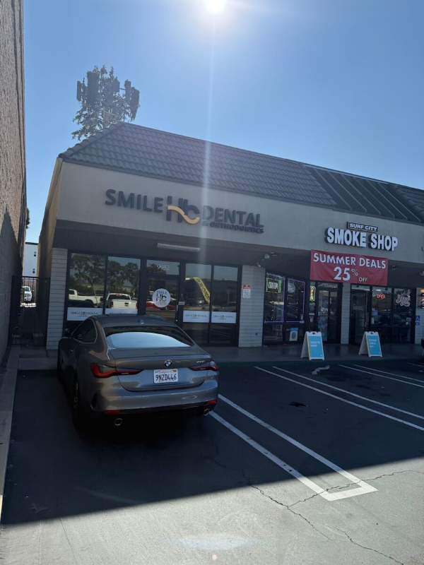 Smile Dental and Smoke Shop storefront with parked car in front, bright sunny day