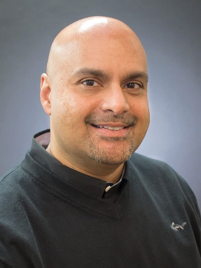 Smiling bald man in a black shirt against a plain gray background