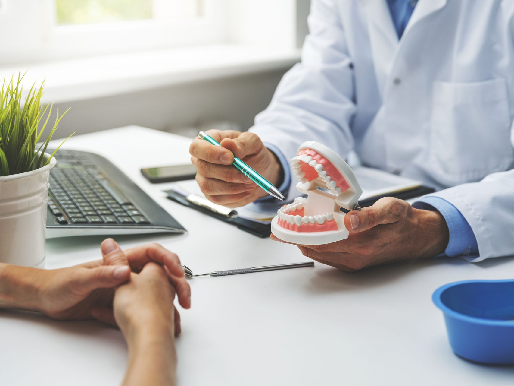 Dentist showing a dental model to a patient during a consultation, with computer and tools on a desk