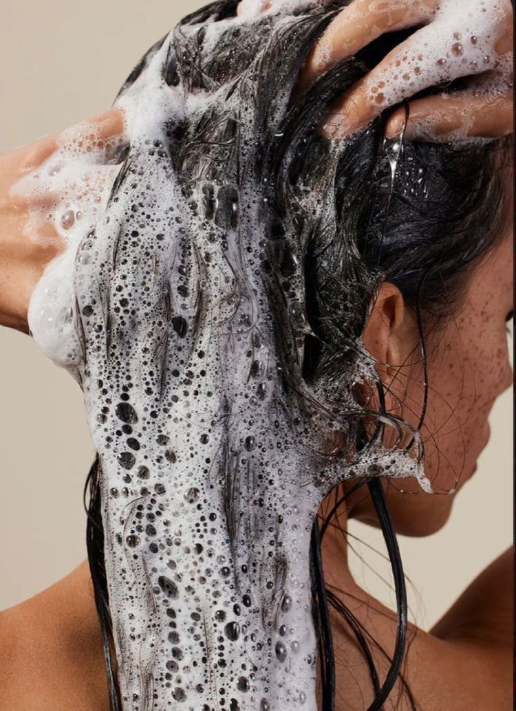 Person washing hair with shampoo lather in a shower