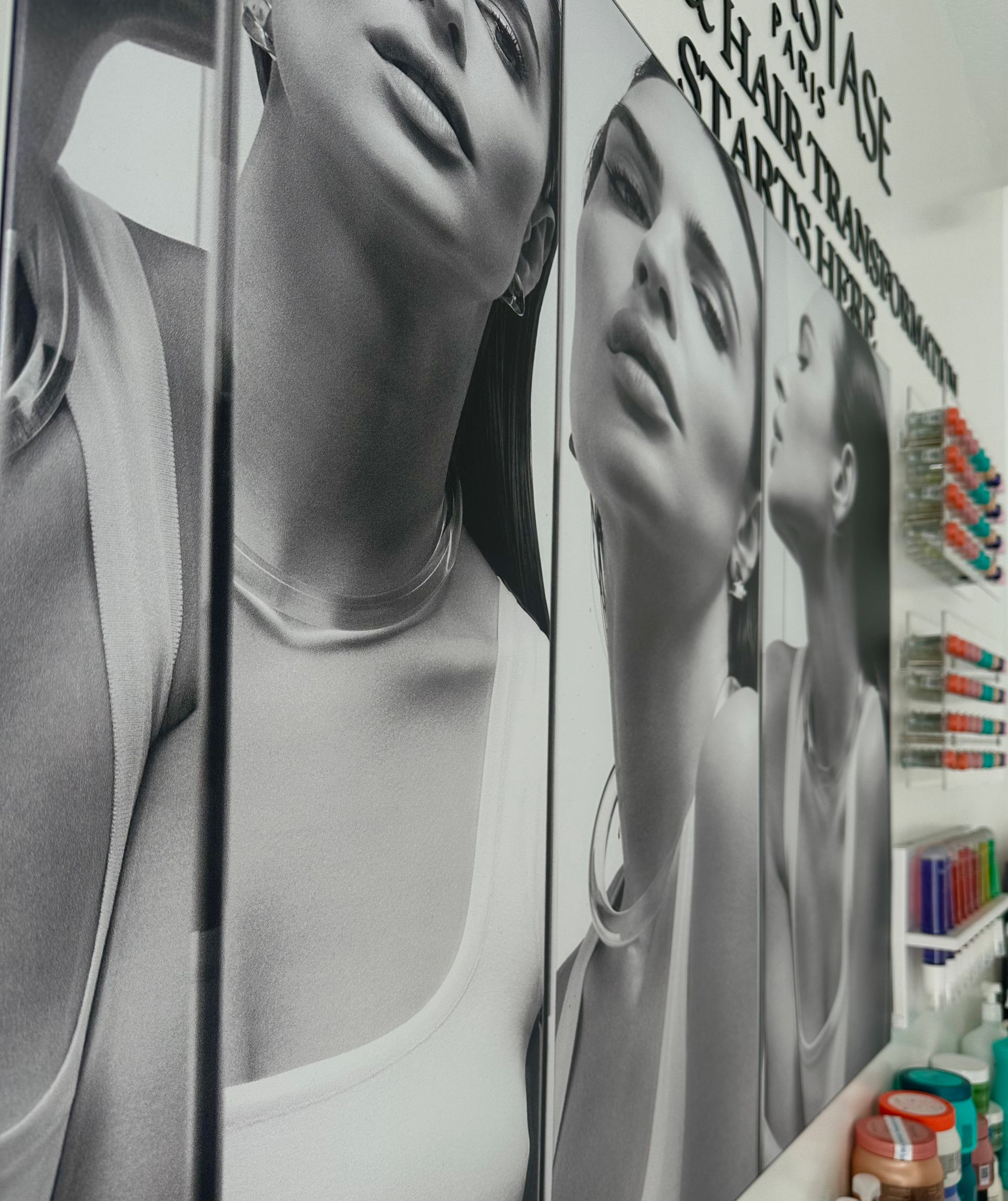 Black-and-white promotional posters of three individuals on a salon wall, with hair products displayed on nearby shelves.