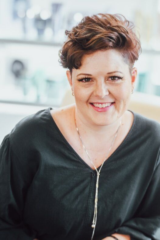 A woman wearing a black shirt and a gold necklace is smiling for the camera.
