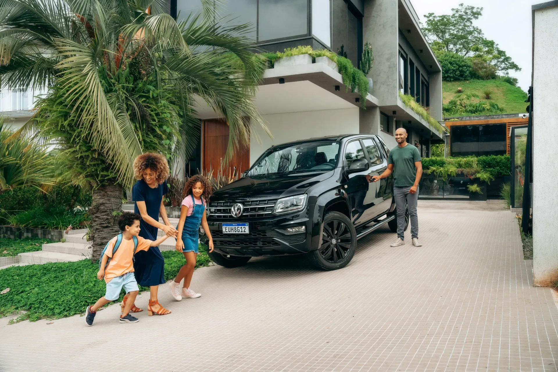 Família ao lado de um SUV preto na entrada de uma casa moderna.