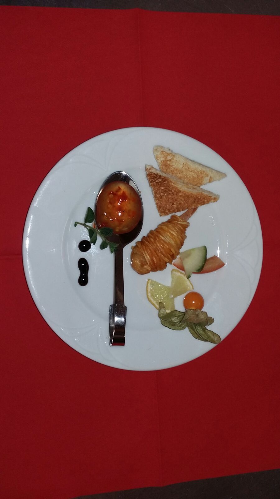 Ein auf einer roten Tischdecke angerichtetes Dessert mit Erdbeeren, Gebäck und einem Löffel.