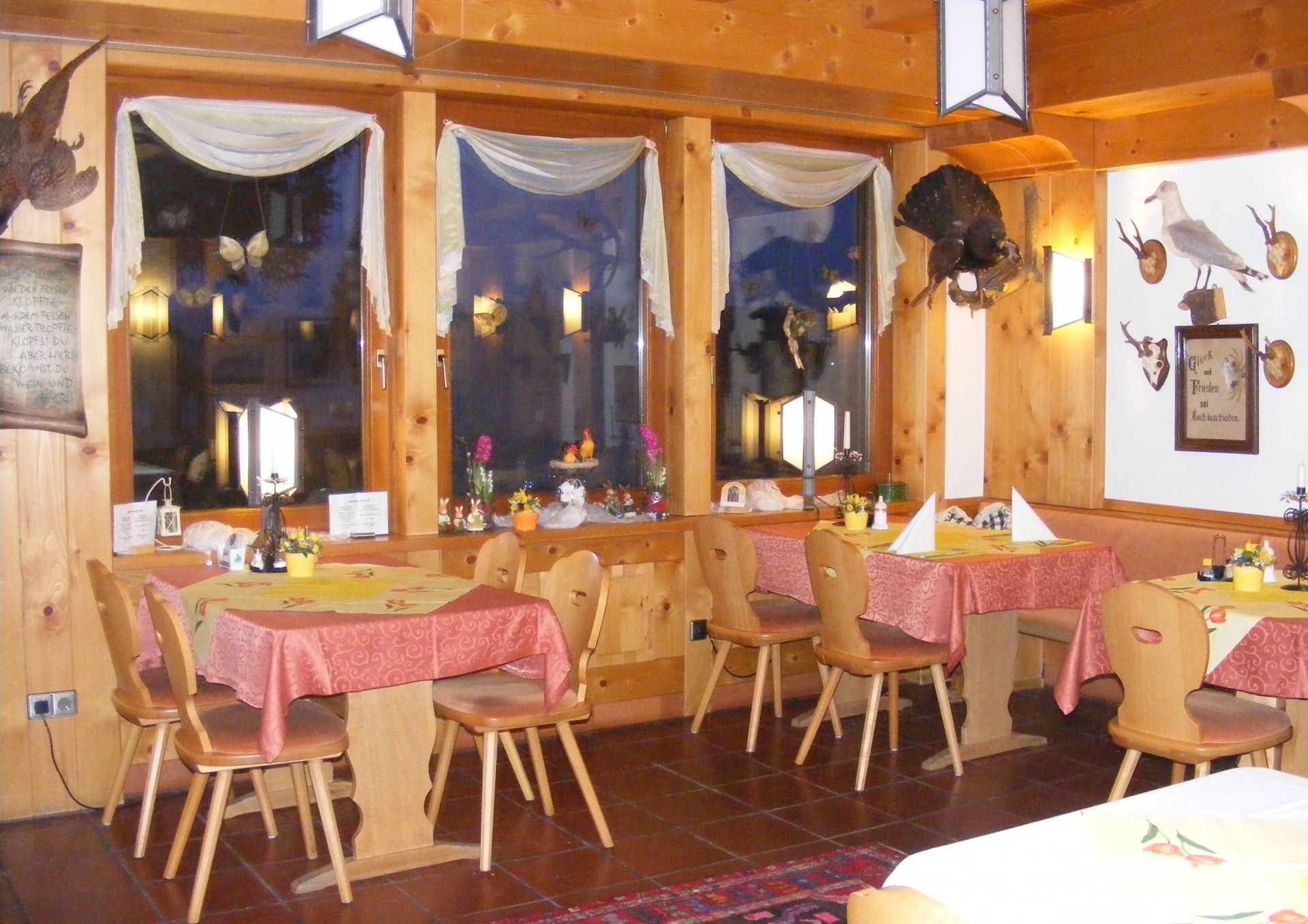 Gemütlicher Speisesaal im Landhausstil mit Holztischen, rosa Tischdecken und Laternen an den verhängten Fenstern