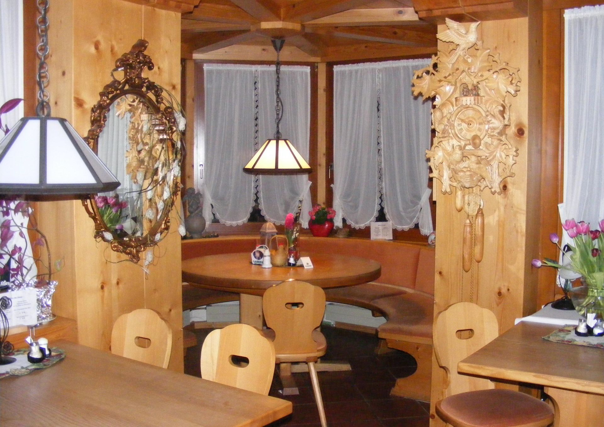 Gemütliches Restaurantinterieur aus Holz mit Sitznischen, Hängelampen, Vorhängen und Blumendekorationen