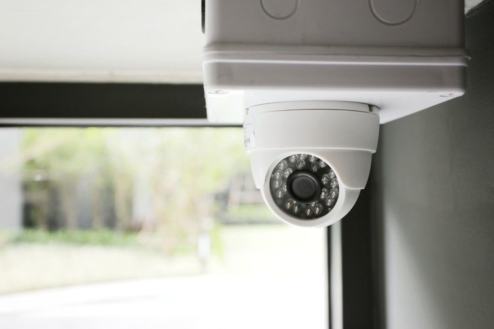 White Security Camera Mounted on A Wall, Facing Forward, with A Window — Ryphen Electrical in Torquay, VIC