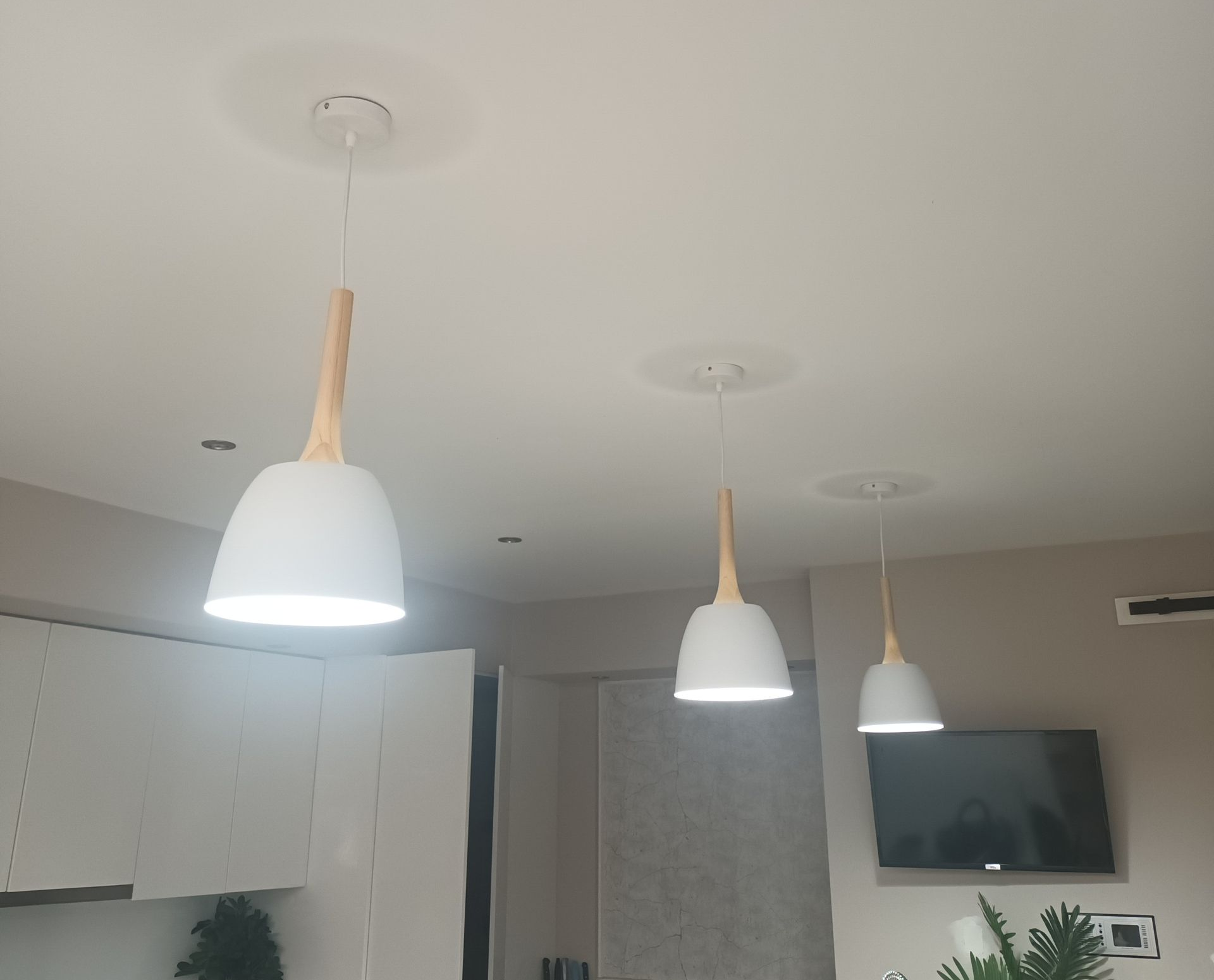 Three white pendant lights with wooden accents hang from a white ceiling, in a room with a TV. — Ryphen Electrical in Highton, VIC