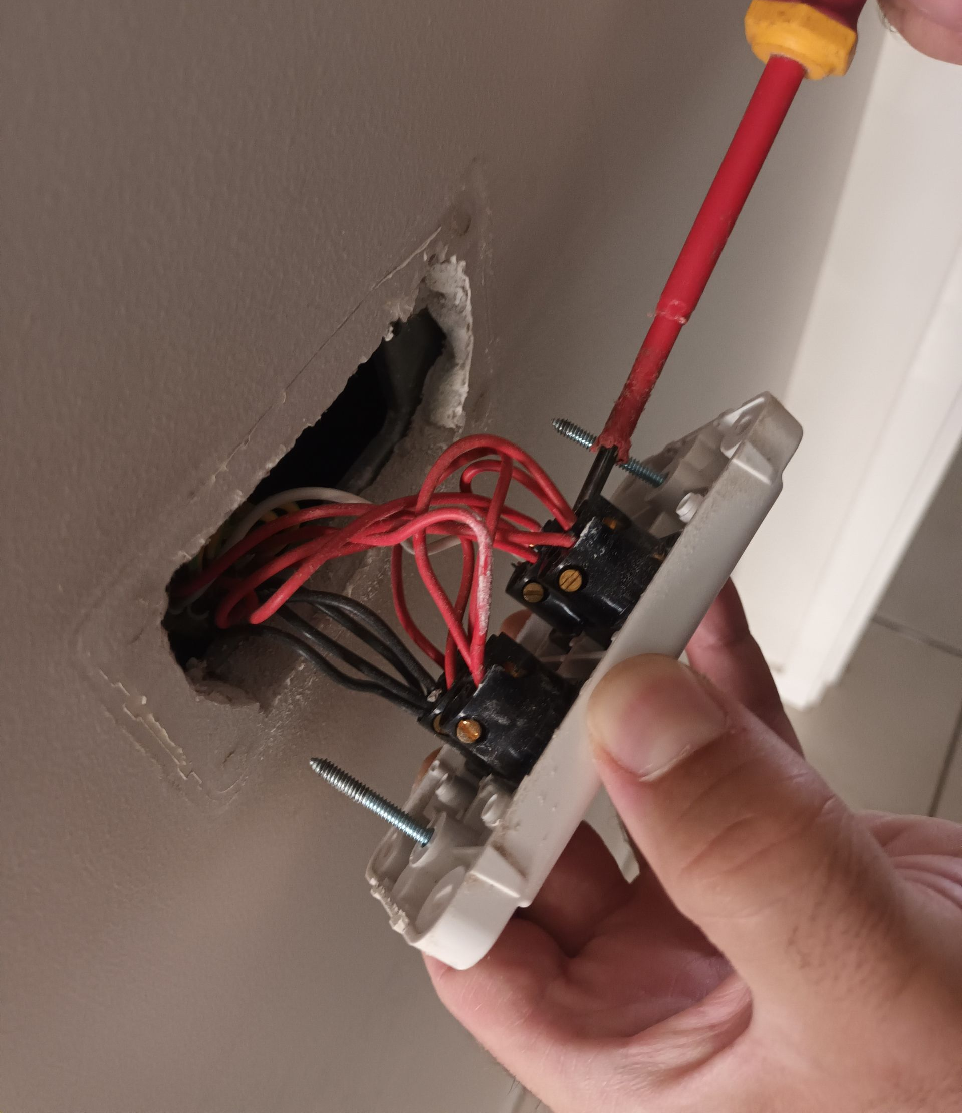 Hand adjusting light switch wires with a screwdriver inside a wall cavity. — Ryphen Electrical in Highton, VIC