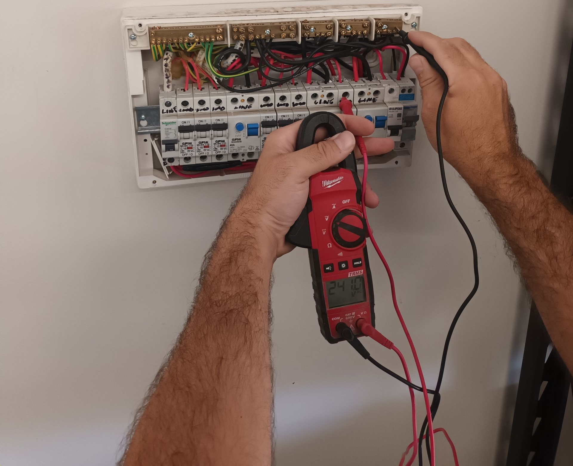 Electrician testing wires in electrical panel with a multimeter. White wall background. — Ryphen Electrical in Highton, VIC