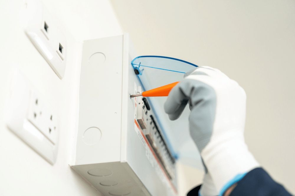 Electrician in White Gloves Uses a Screwdriver on a White Electrical Box on a Wall — Ryphen Electrical in Highton, VIC