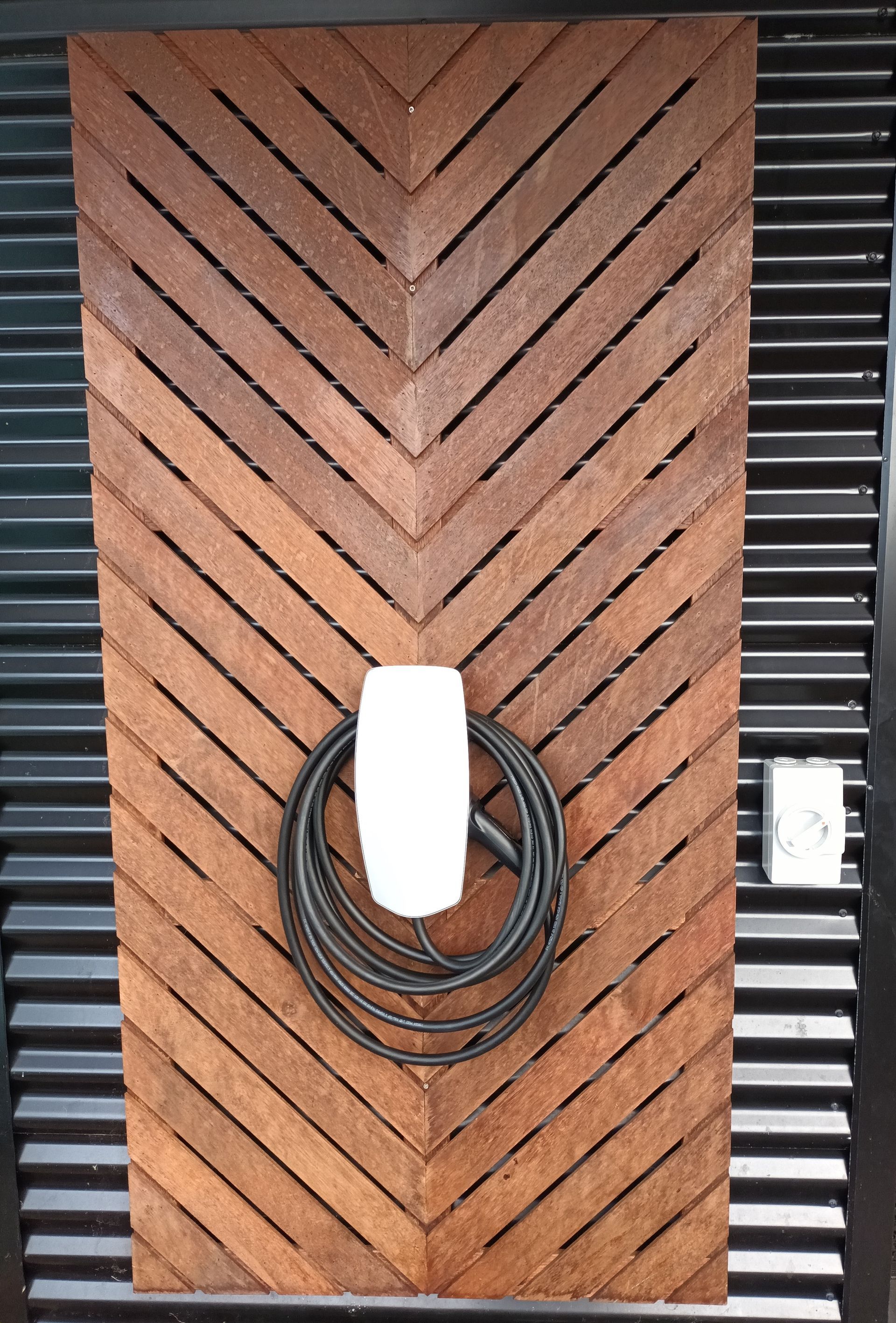 Wooden chevron-patterned wall with an electric car charger and a coiled black cable. — Ryphen Electrical in Highton, VIC