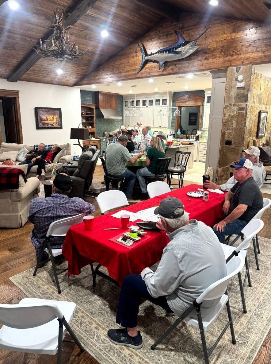 People seated at red-covered tables in a rustic dining room, gathered for a meal or meeting