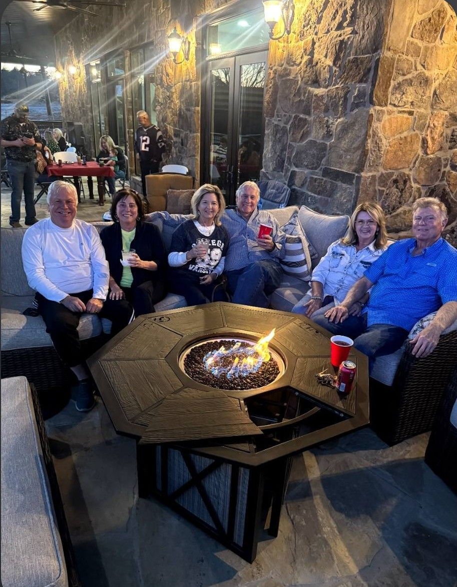 Group seated around a fire pit on an outdoor patio at night, holding drinks and smiling.