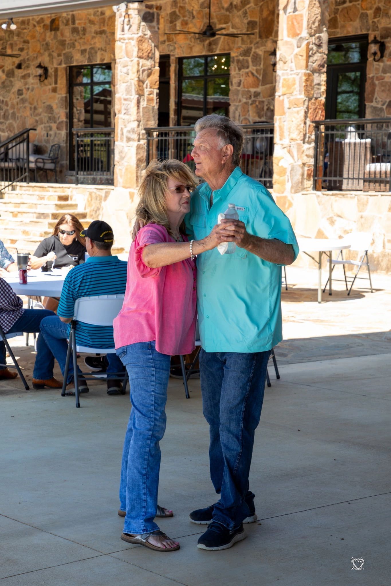 Two people dancing closely in a covered outdoor patio, one in pink and one in turquoise.