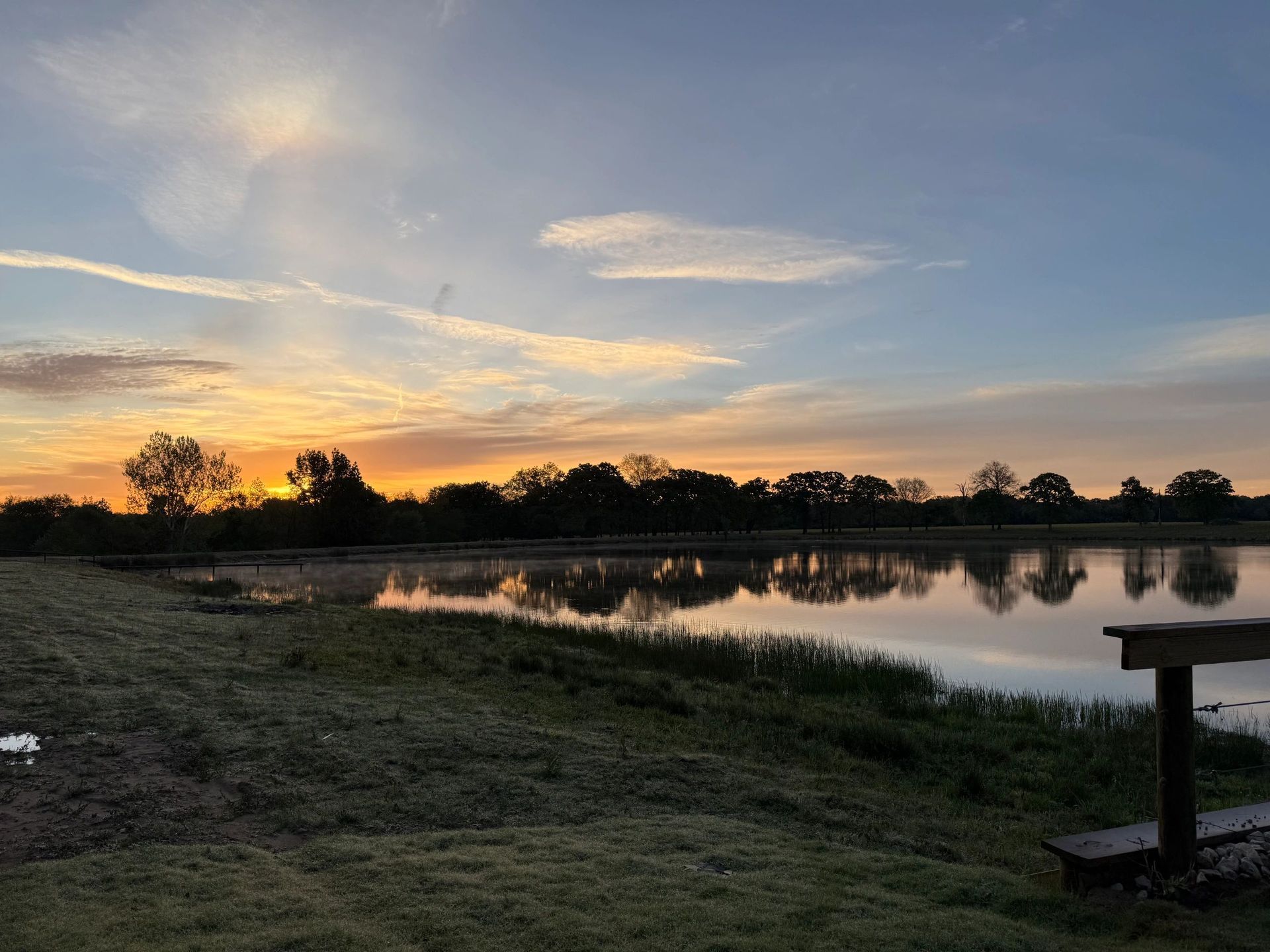 Sunset over a calm lake with silhouetted trees and a small dock in the foreground