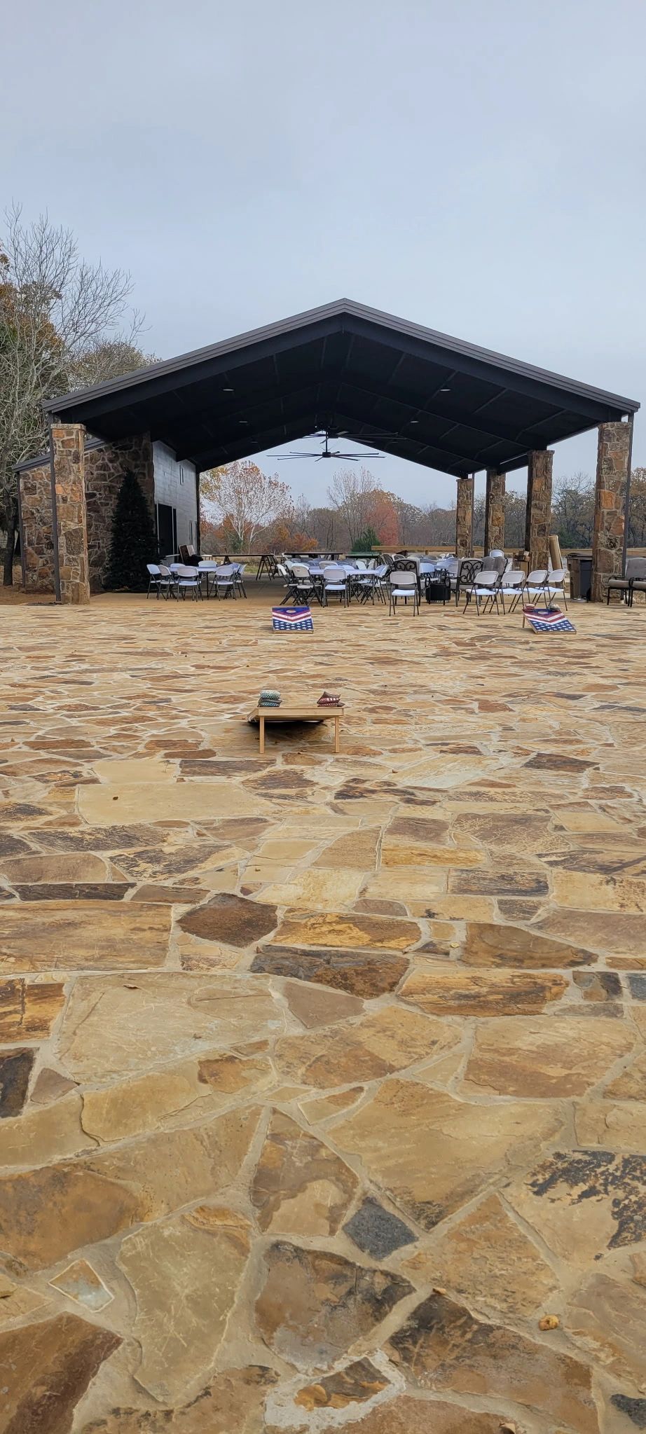 Open-air pavilion on a stone patio with picnic tables and trees in the background