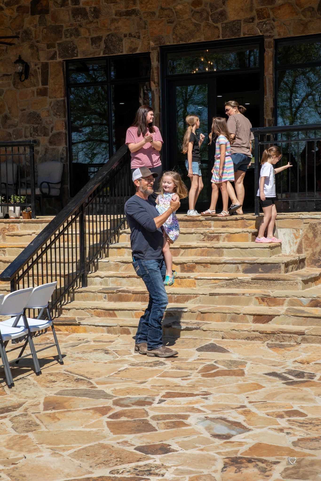 Group of people standing on stone steps outside a rustic building, with a man in the foreground holding a camera.