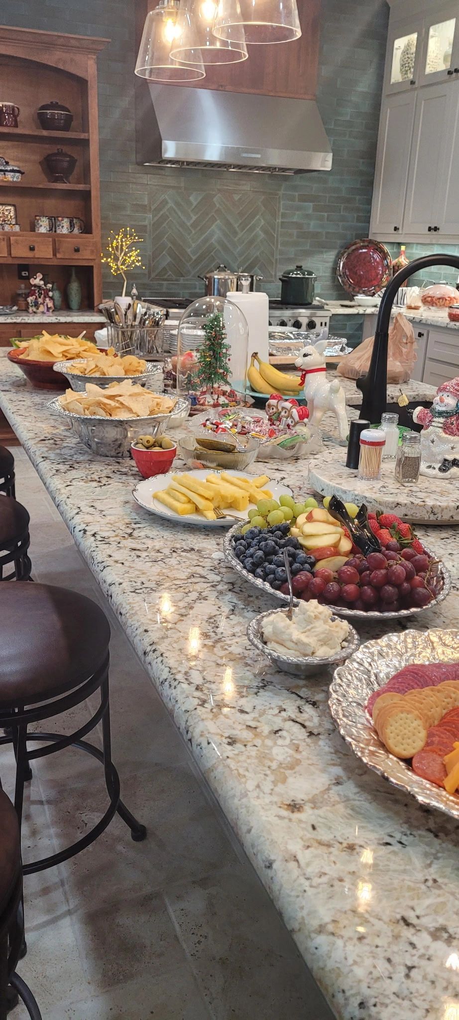 Buffet spread on a granite kitchen island with fruit, pastries, and snacks in a warm, modern room