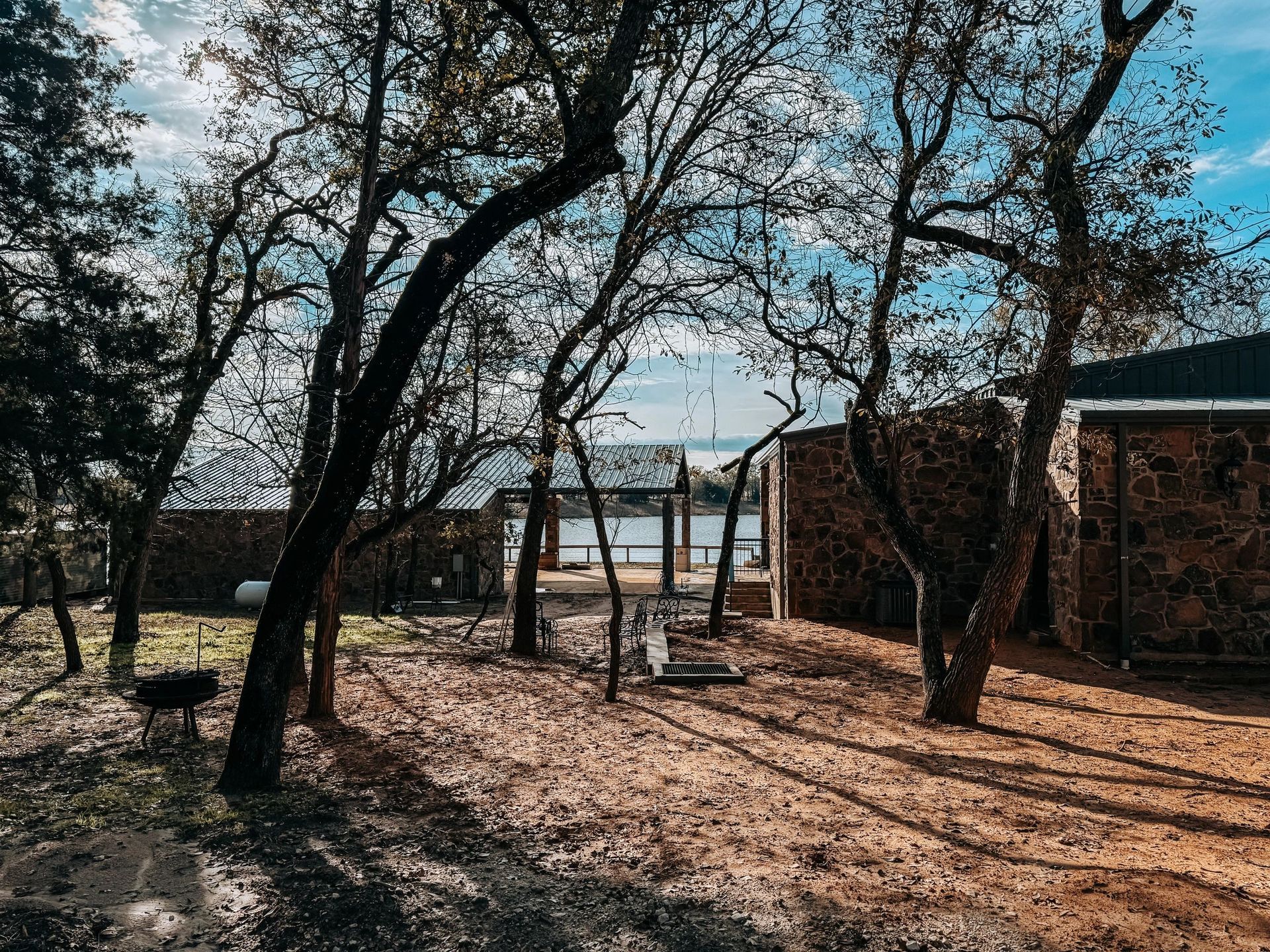 Shaded backyard with trees, a swing set, and a brick building under a bright blue sky