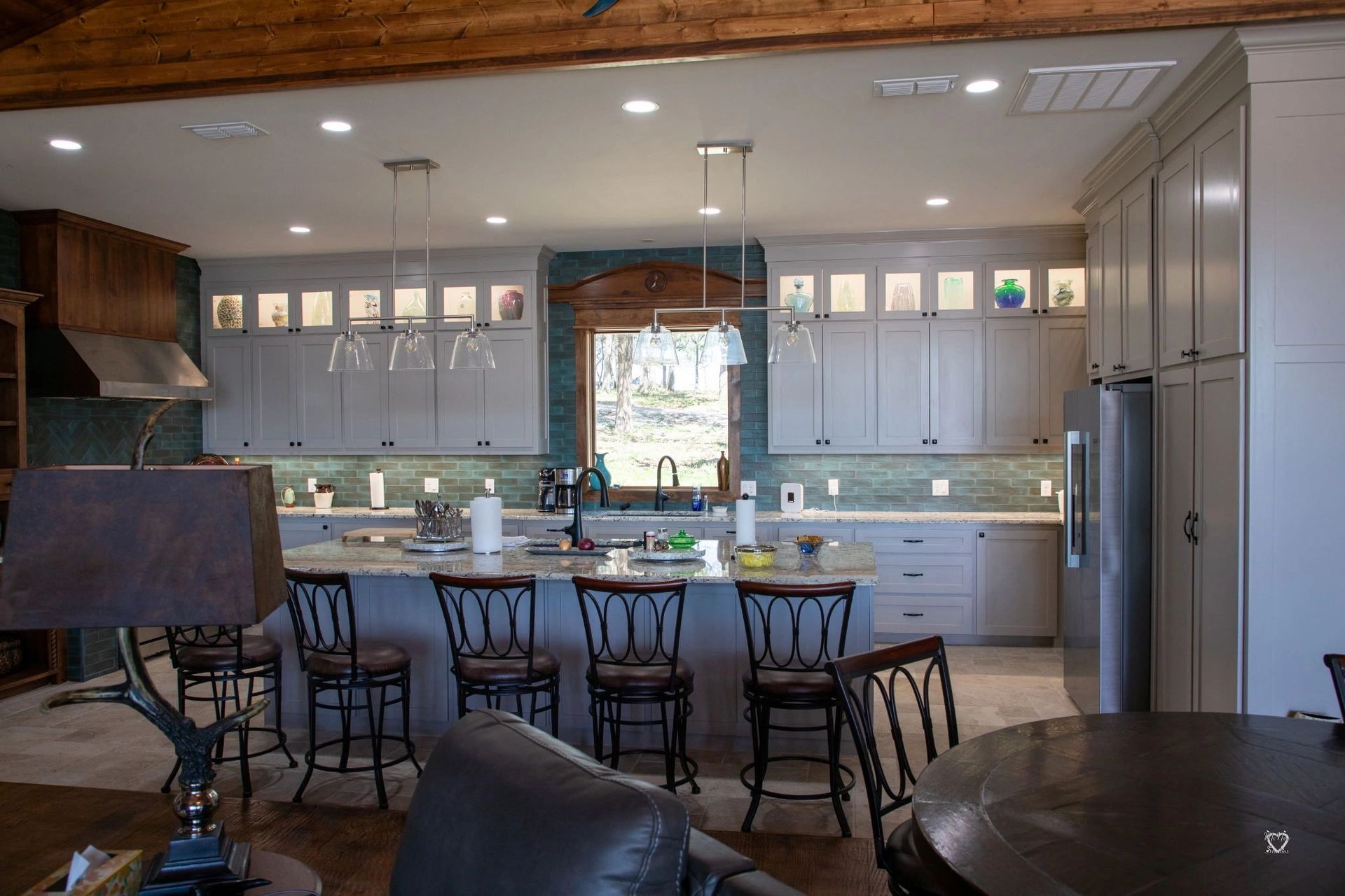 Modern kitchen with island, bar stools, white cabinets, and stainless steel refrigerator beneath wood ceiling