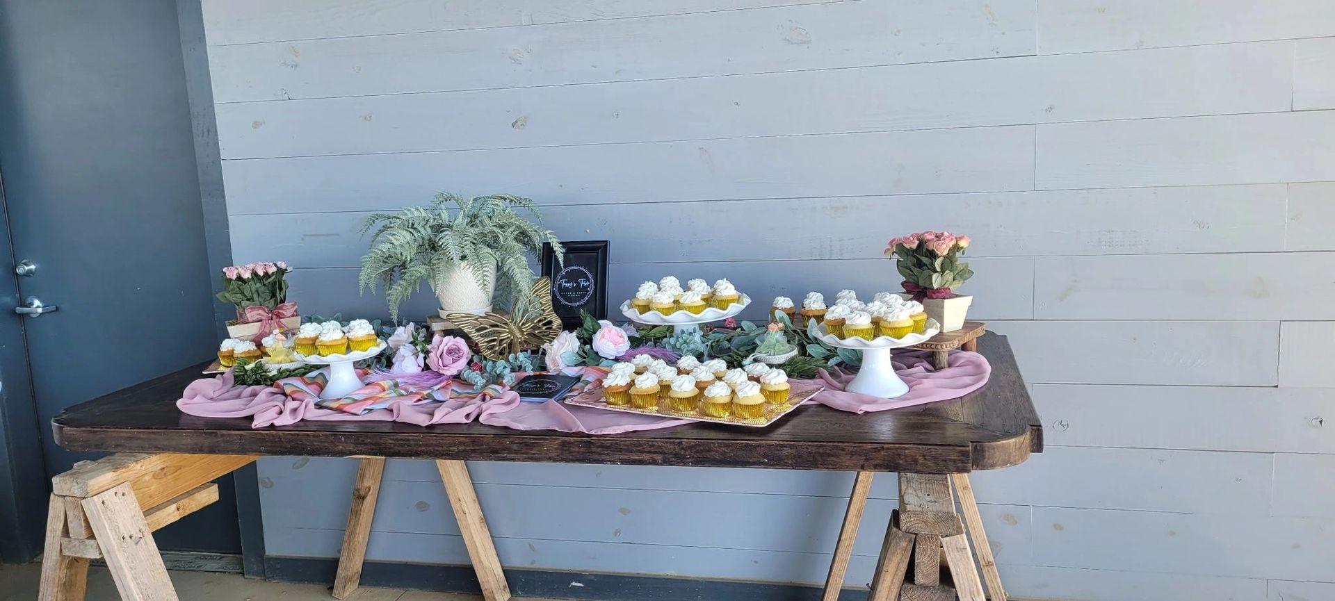 Outdoor table display with flowers and cupcakes against a gray wall