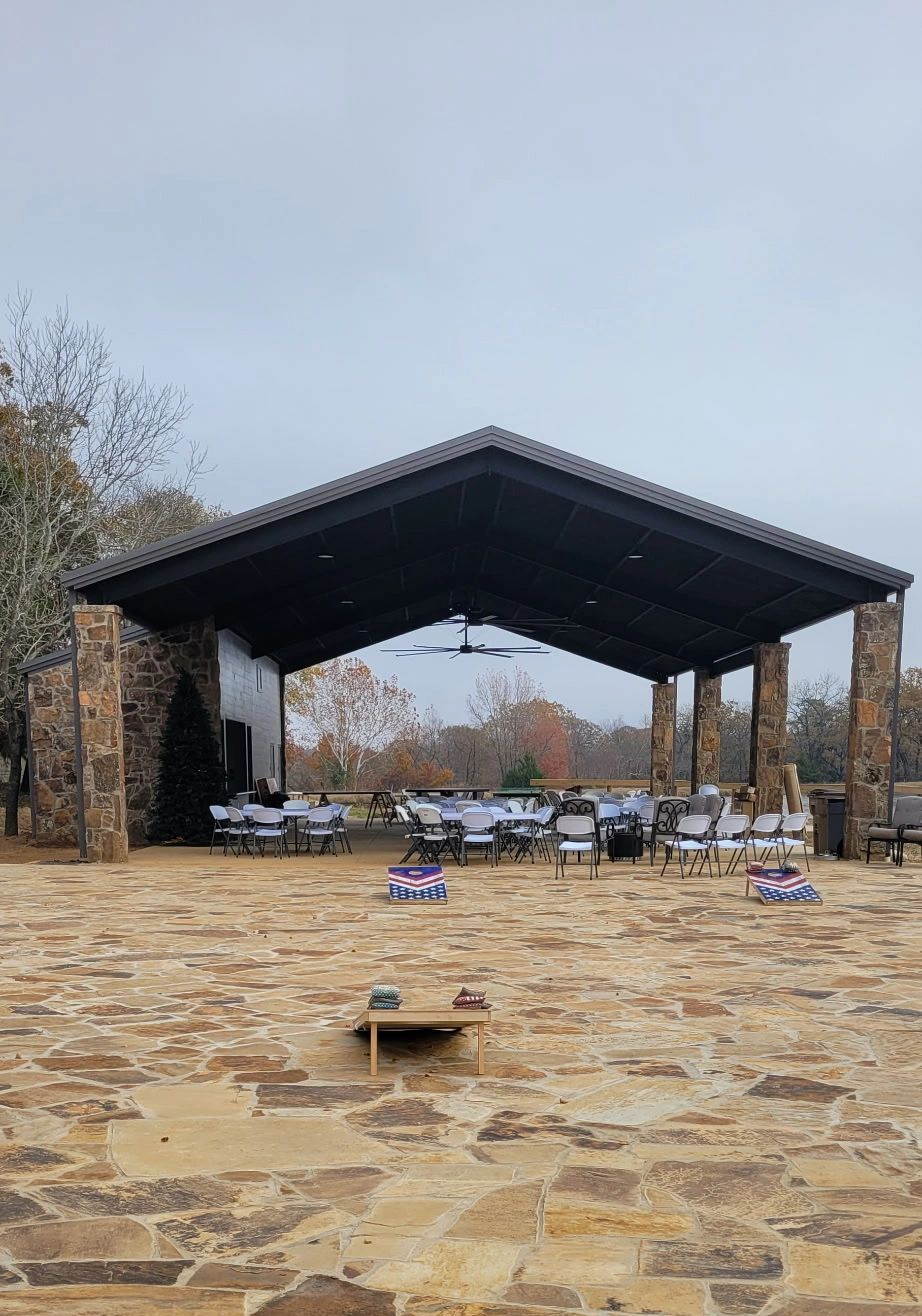 Stone pavilion with picnic tables and benches on a paved plaza under a gray sky