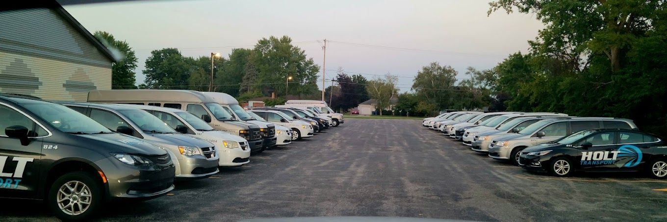 Parking lot lined with parked cars on both sides of a gravel road at dusk