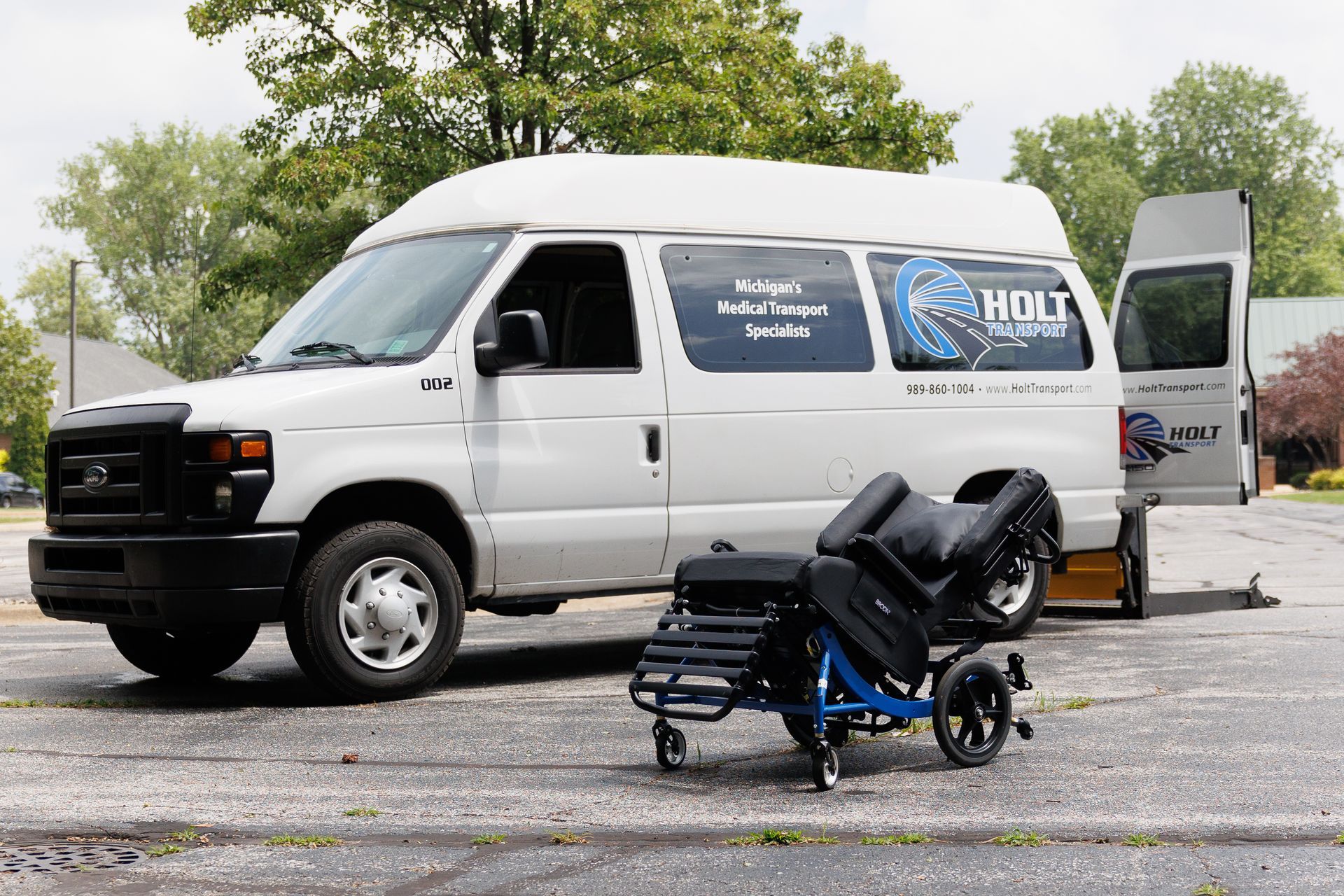 White van parked outdoors with a folded wheelchair on a small cart in front of it