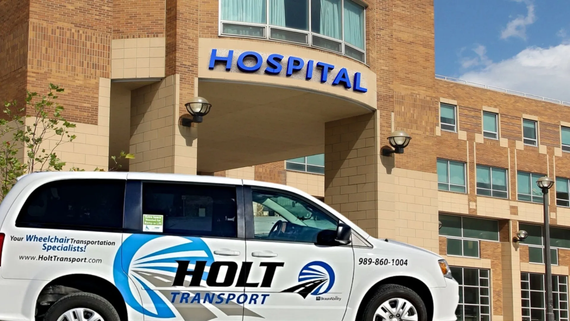 A holt transport van is parked in front of a hospital