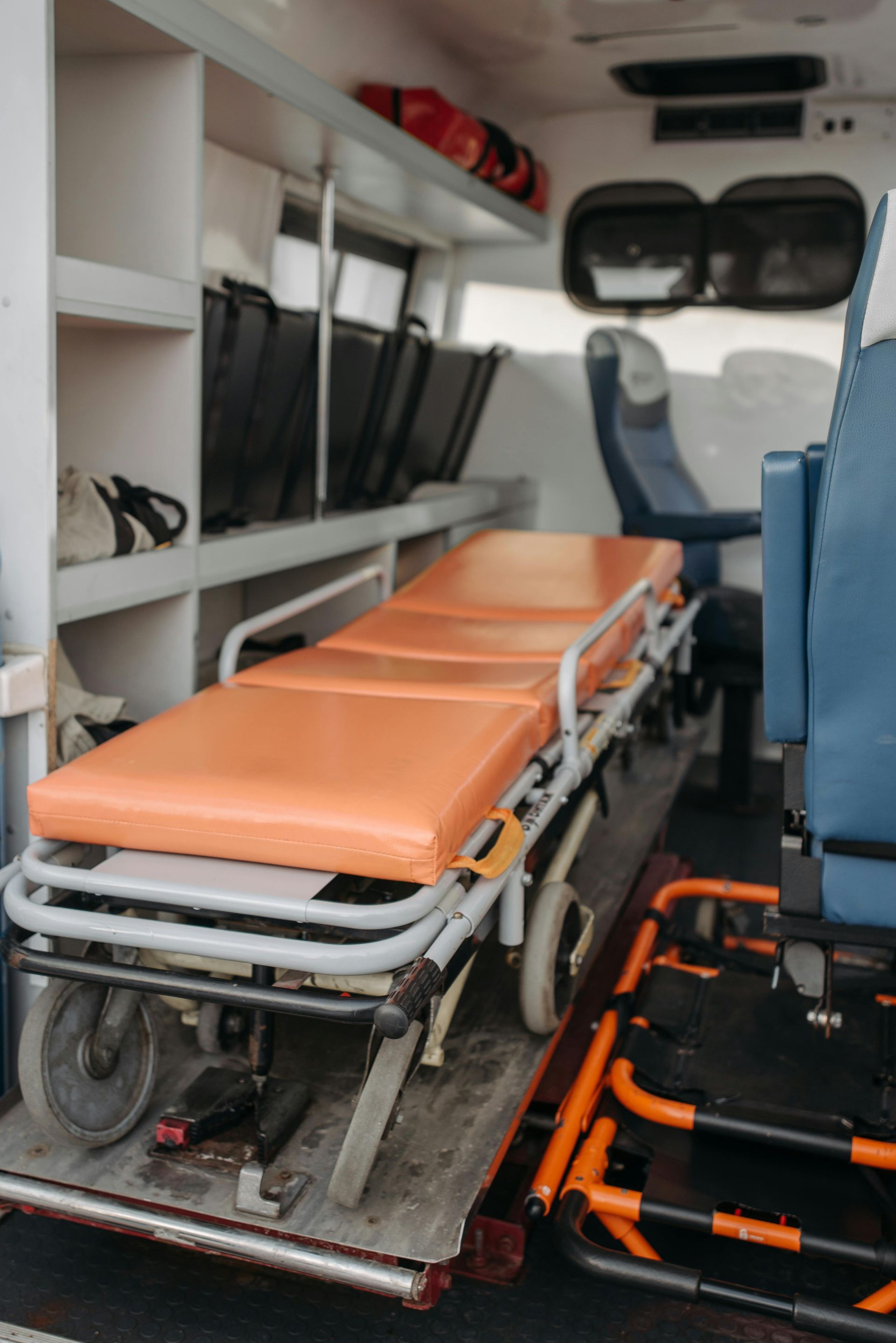 The interior of an ambulance featuring an orange stretcher and a blue attendant chair.