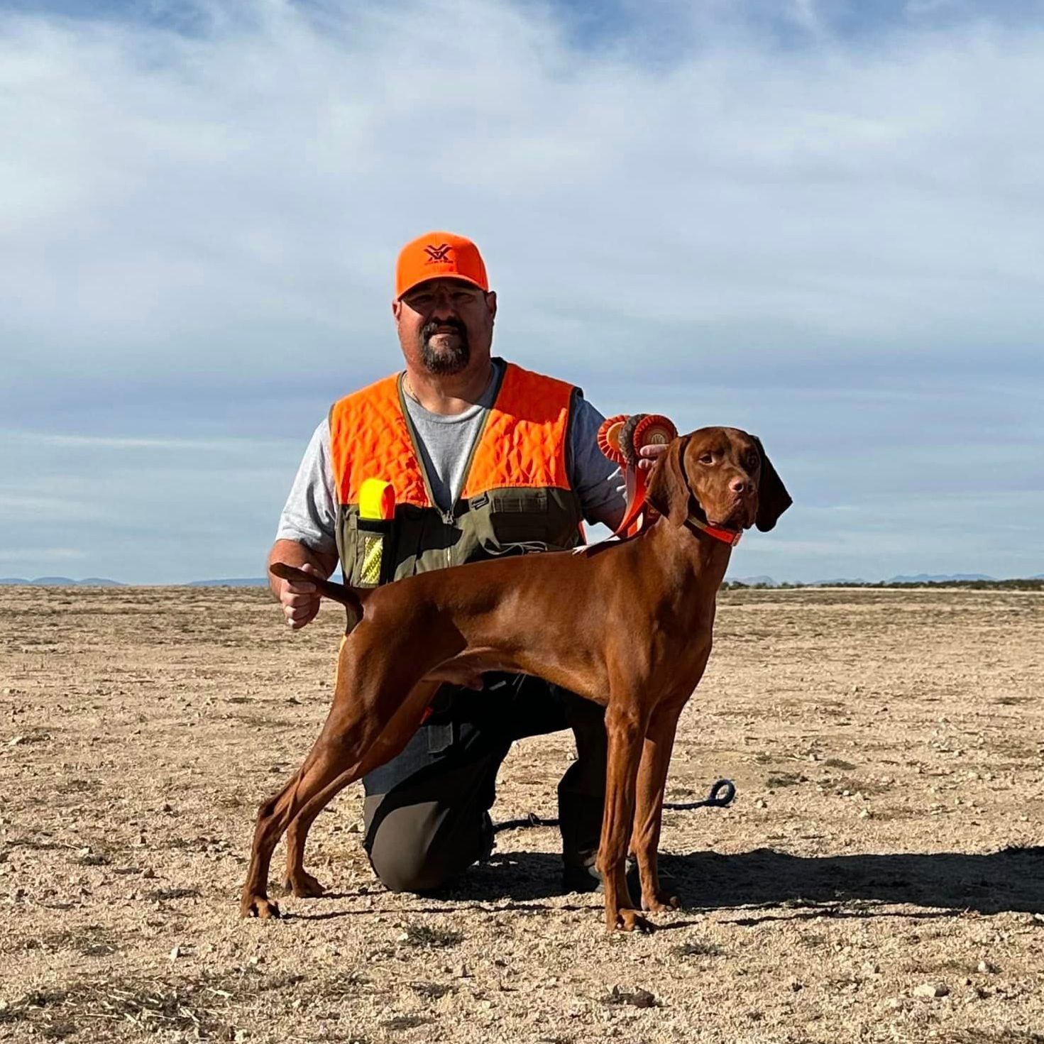 A man is kneeling down next to a brown dog in a field.