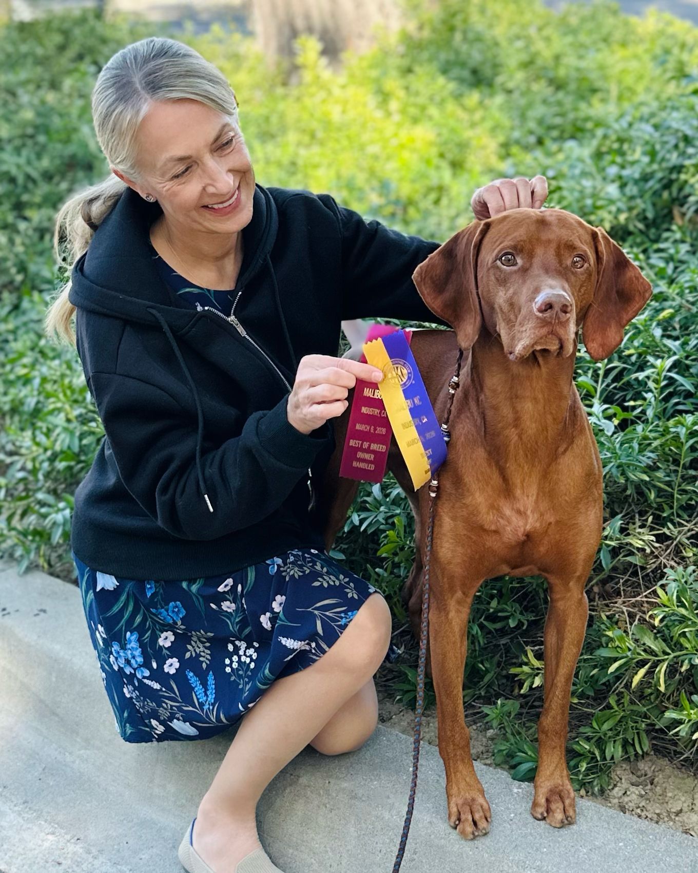 A woman is standing next to a dog on a podium with ribbons.