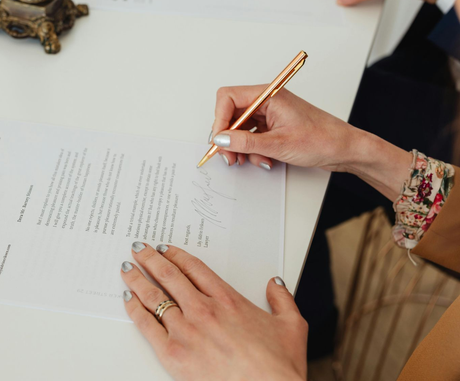 Person signing a document with a gold pen, silver nails, and floral bracelet.