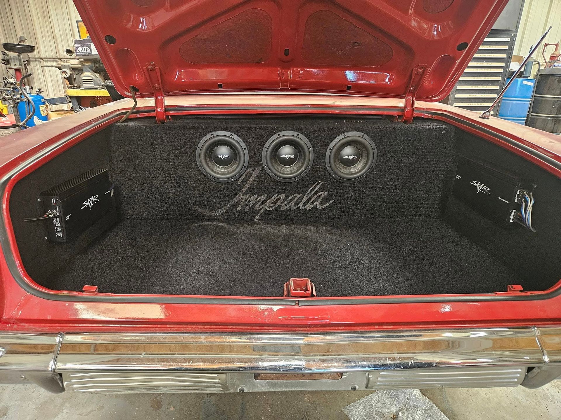 Open car trunk with custom black speaker panel in a red vehicle
